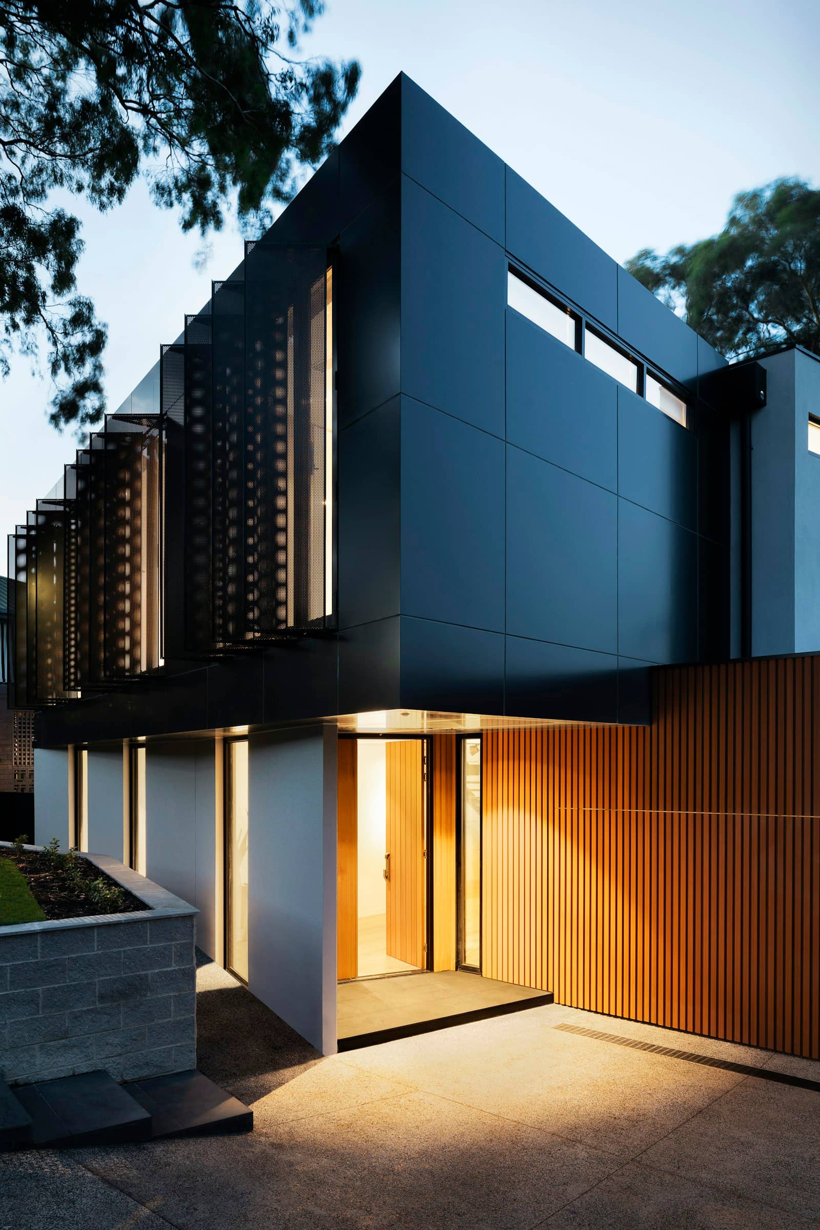 Free-license stock photograph — a dark timber facade at dusk, warm light falling through the slatted entry. Illustrative: no photograph on this site shows built work.